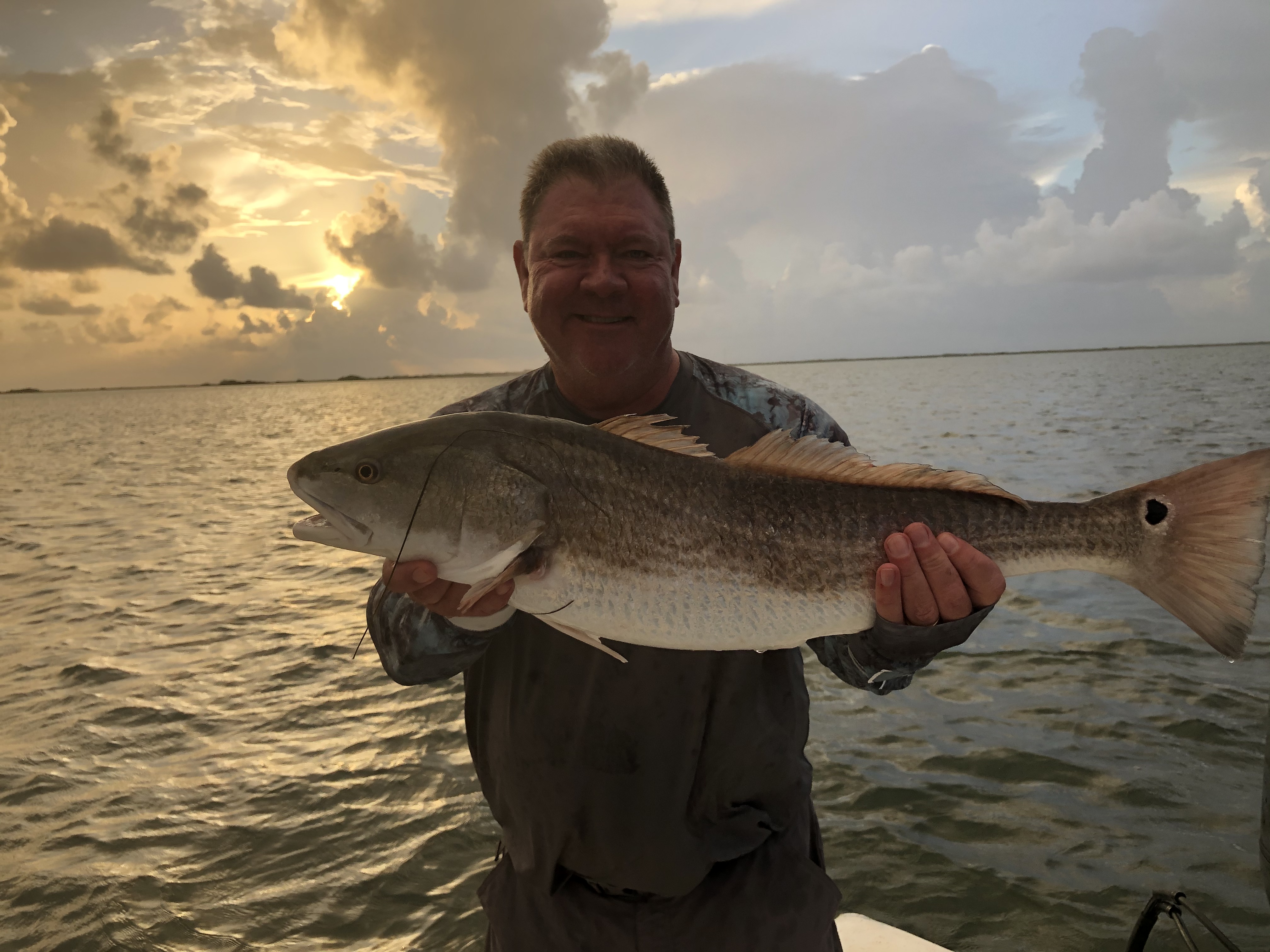 An angler holding a redfish on the water at sunrise